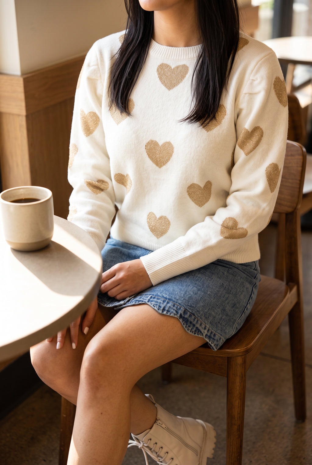 Seated coffee-date styling of the Make Me Feel Golden Heart Sweater showing its relaxed fit in Small.