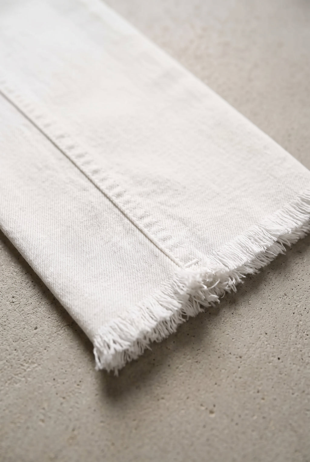 Close detail of All of Me white jeans showing the denim twill, seam stitching and raw frayed hem.