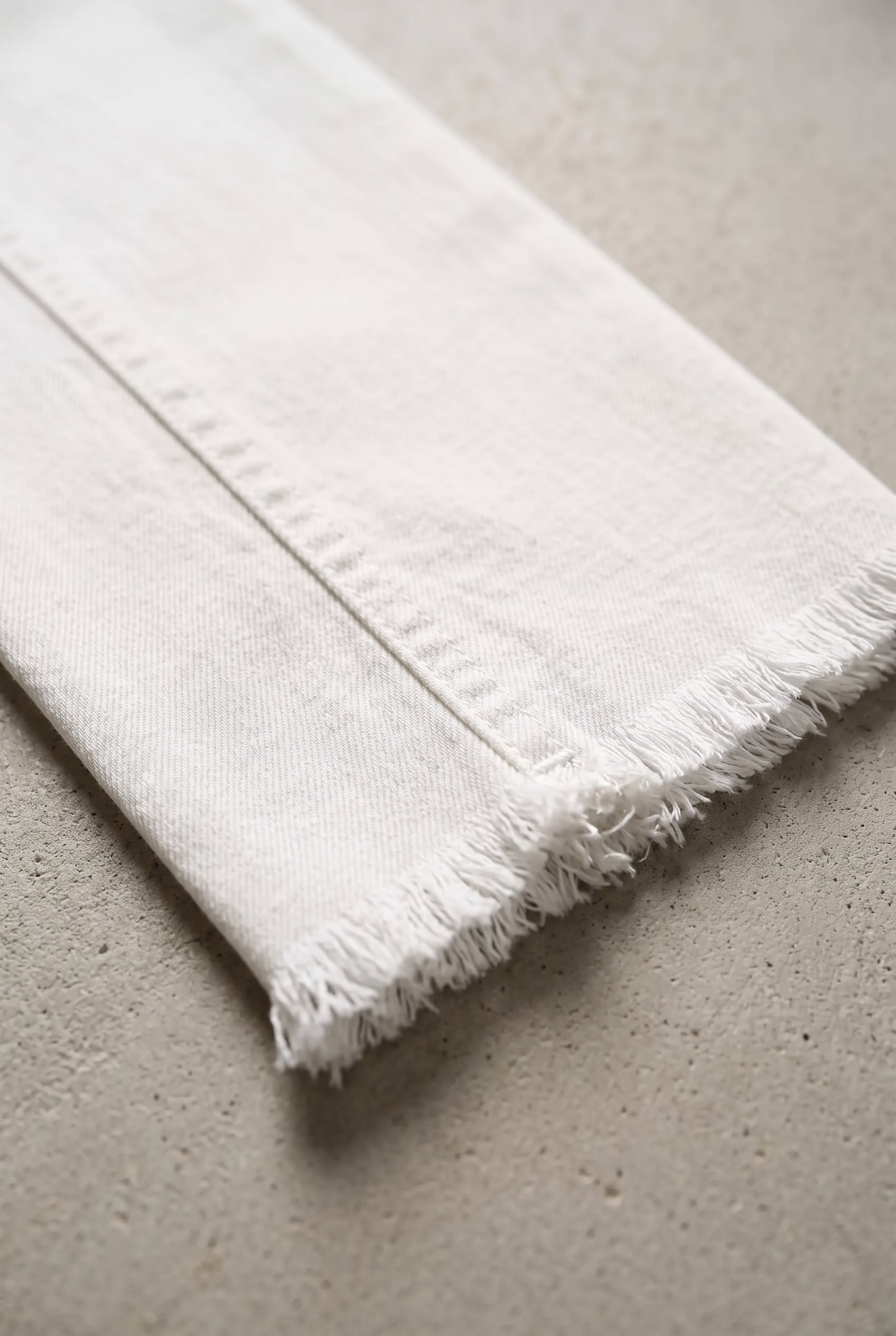 Close detail of All of Me white jeans showing the denim twill, seam stitching and raw frayed hem.