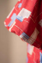 Close detail of the red geometric print, brushed fabric surface and sleeve stitching.