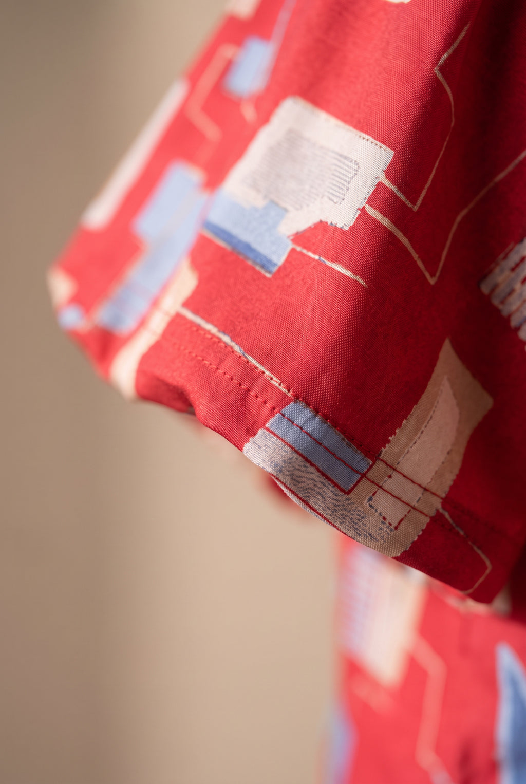 Close detail of the red geometric print, brushed fabric surface and sleeve stitching.