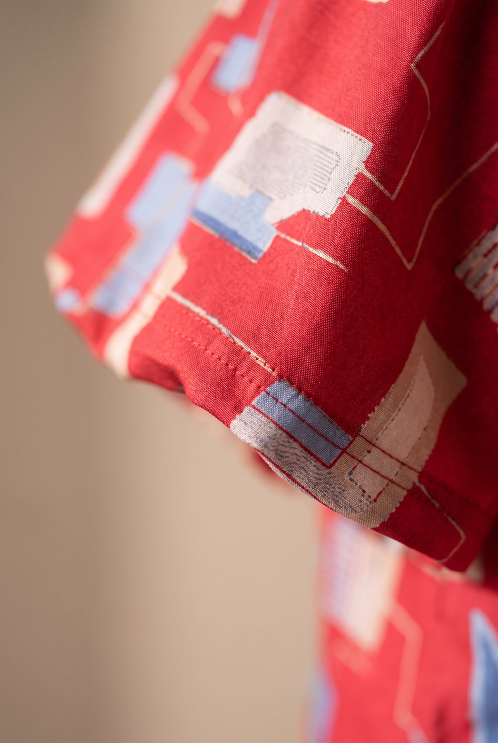 Close detail of the red geometric print, brushed fabric surface and sleeve stitching.