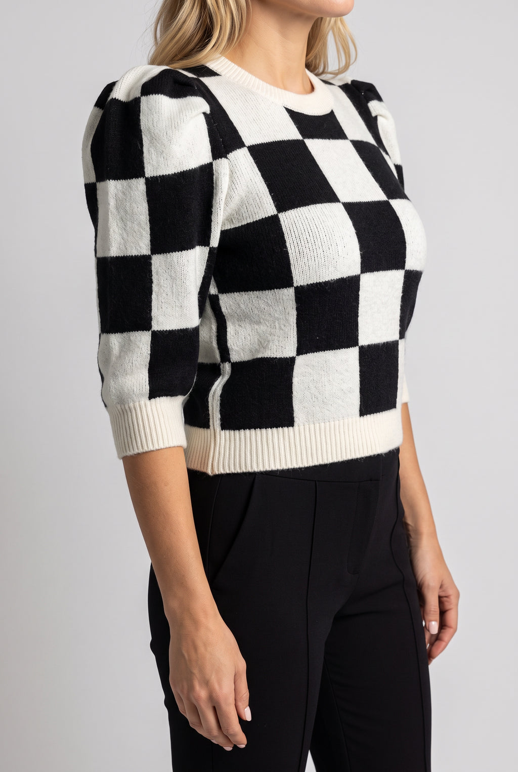 Side fit of the Checkmate Chic sweater showing puff-sleeve depth and the natural ribbed hem.
