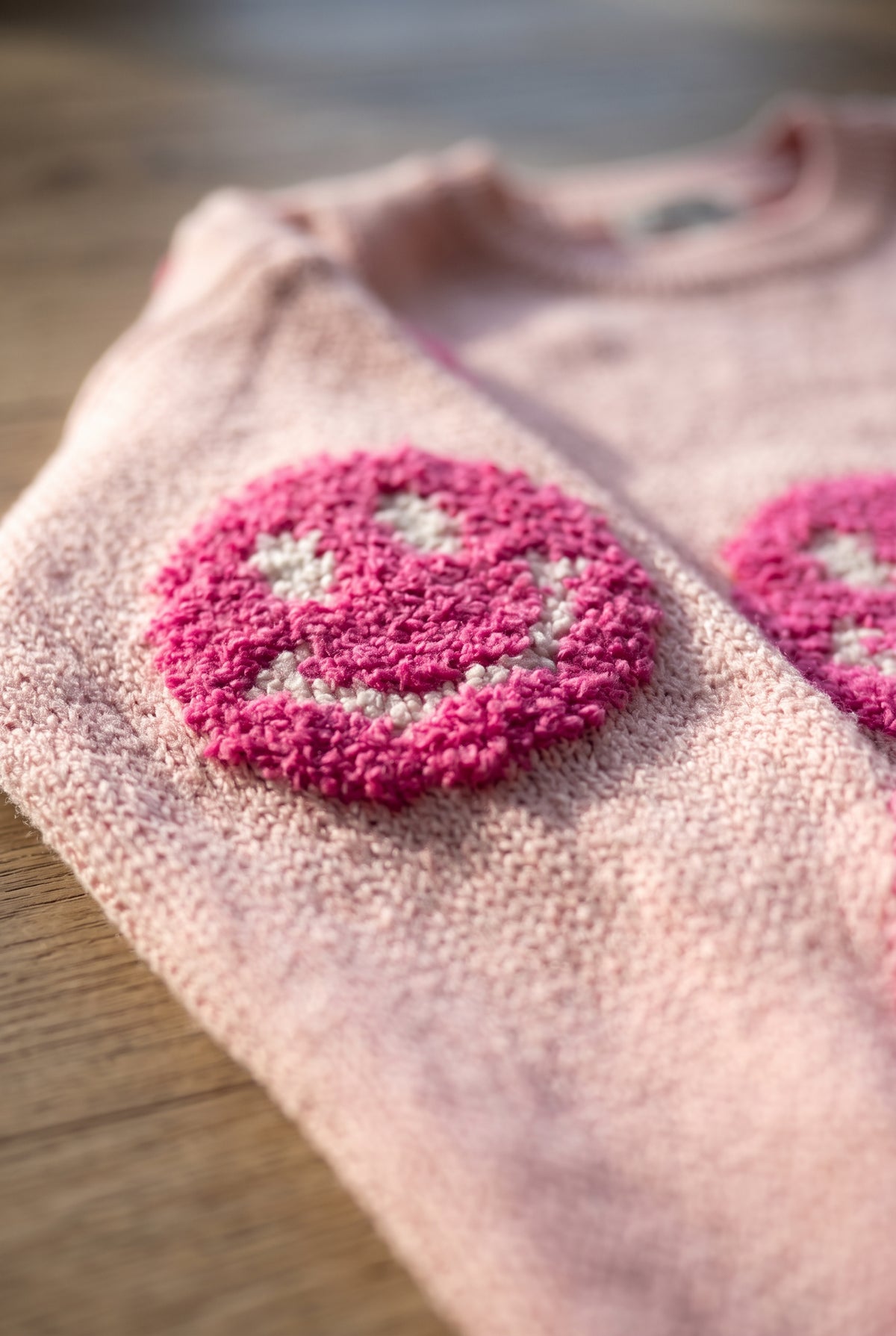 Close detail of the pink happy face sweater showing fuzzy smiley pile, white stitching and base knit.