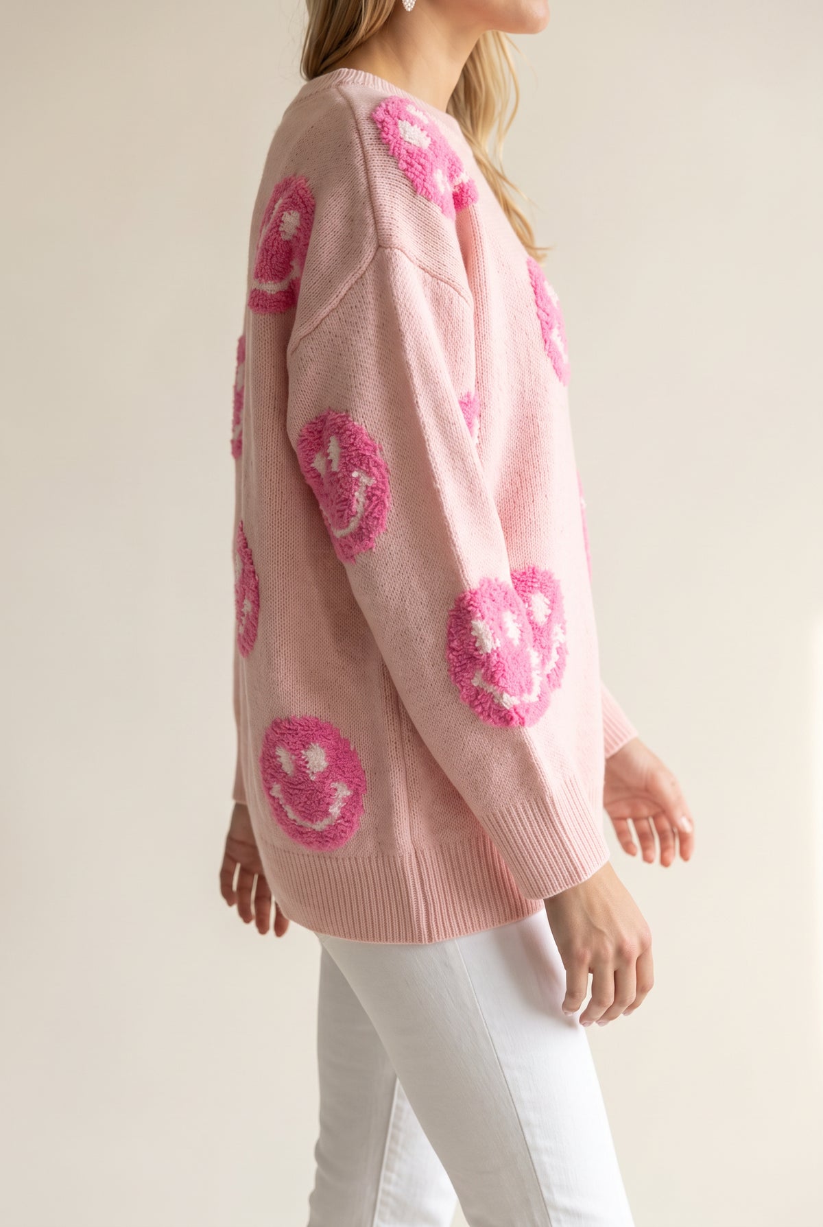 Angled side fit of the pink happy face sweater showing body depth, hip length and roomy sleeves.