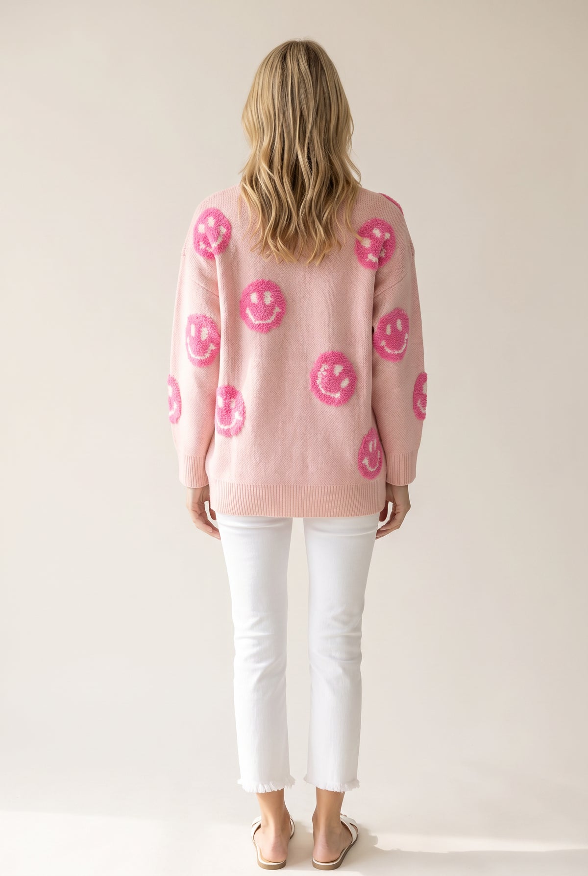 Back fit of the pink happy face sweater showing its untucked hem, dropped shoulders and sleeve volume.