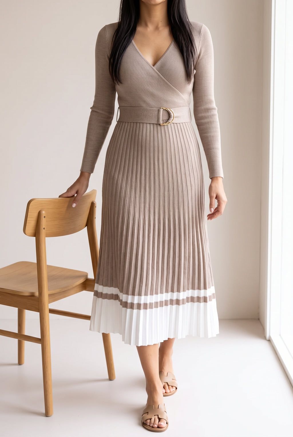 Shweta wears the Small beige pleated sweater dress beside a dining chair for scale.