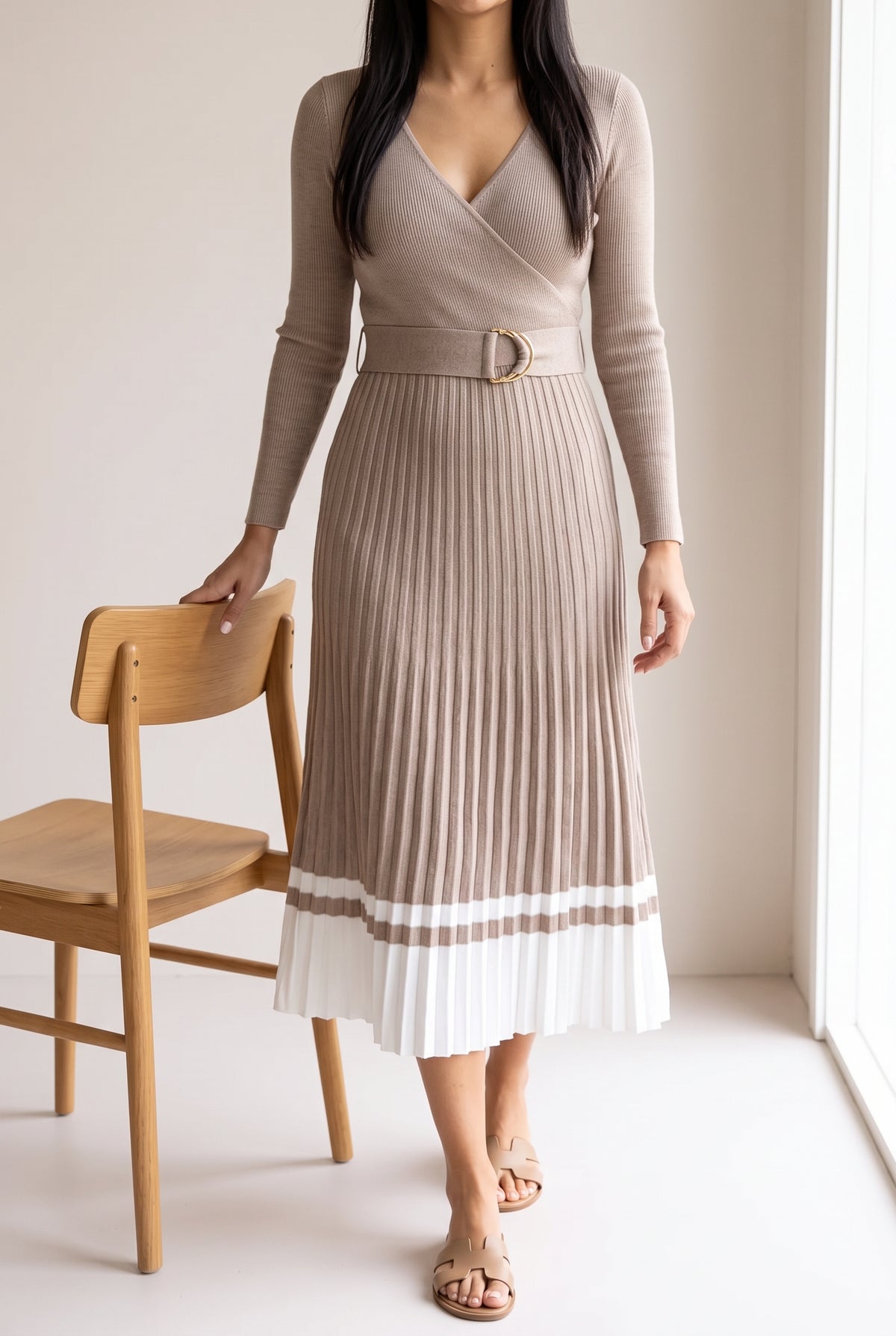 Shweta wears the Small beige pleated sweater dress beside a dining chair for scale.