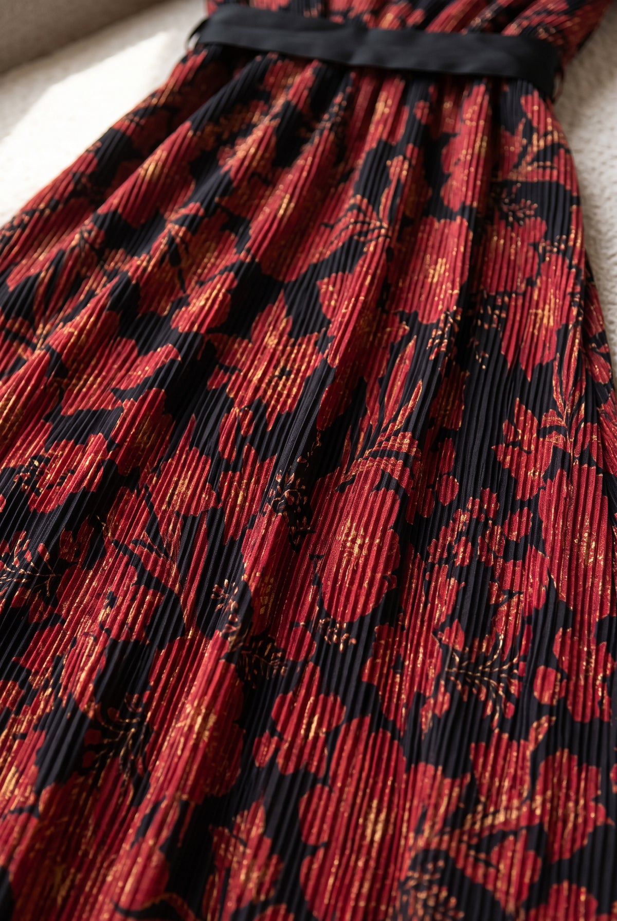 Close detail of the red floral print and fine vertical pleats on the black maxi dress.