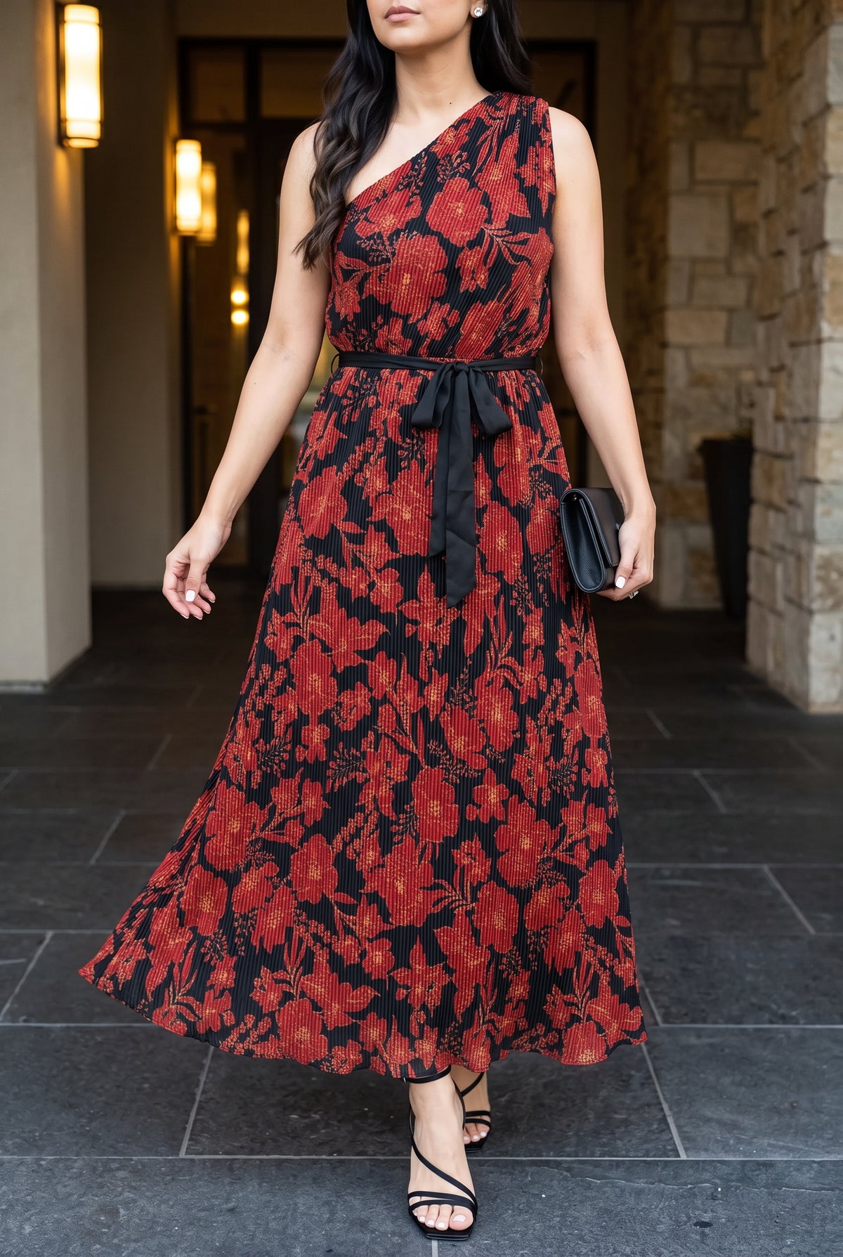 Floral pleated one-shoulder maxi dress styled with black heels and clutch for an evening occasion.