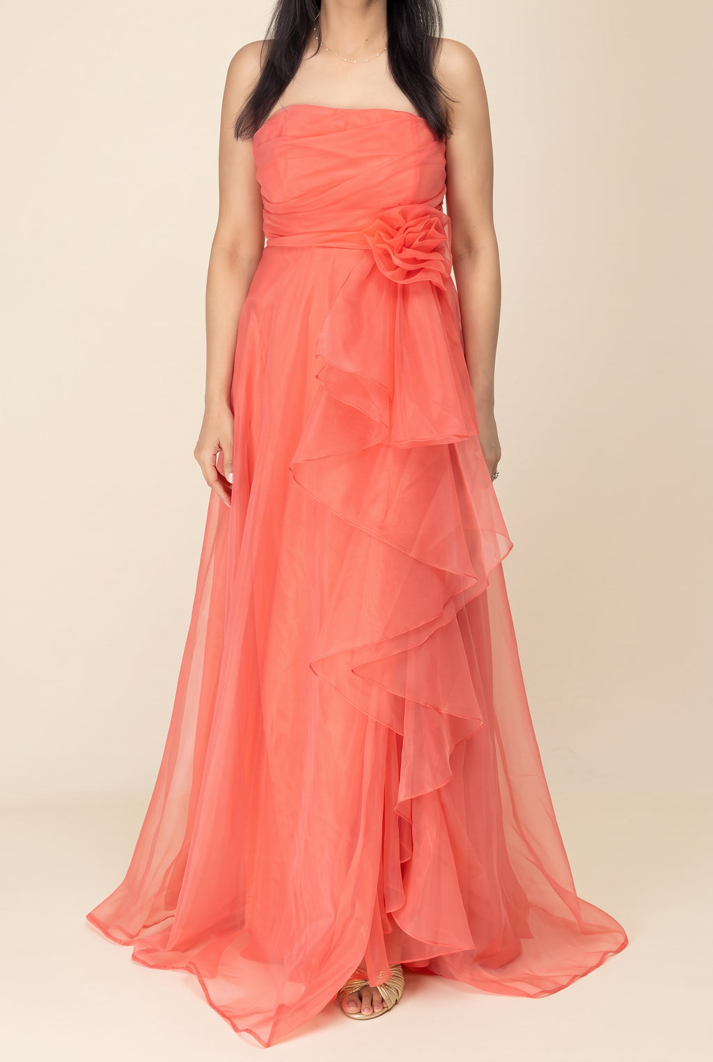 Front view of the coral organza maxi dress showing its strapless bodice, waist flower and full layered skirt.