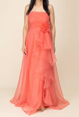 Front view of the coral organza maxi dress showing its strapless bodice, waist flower and full layered skirt.