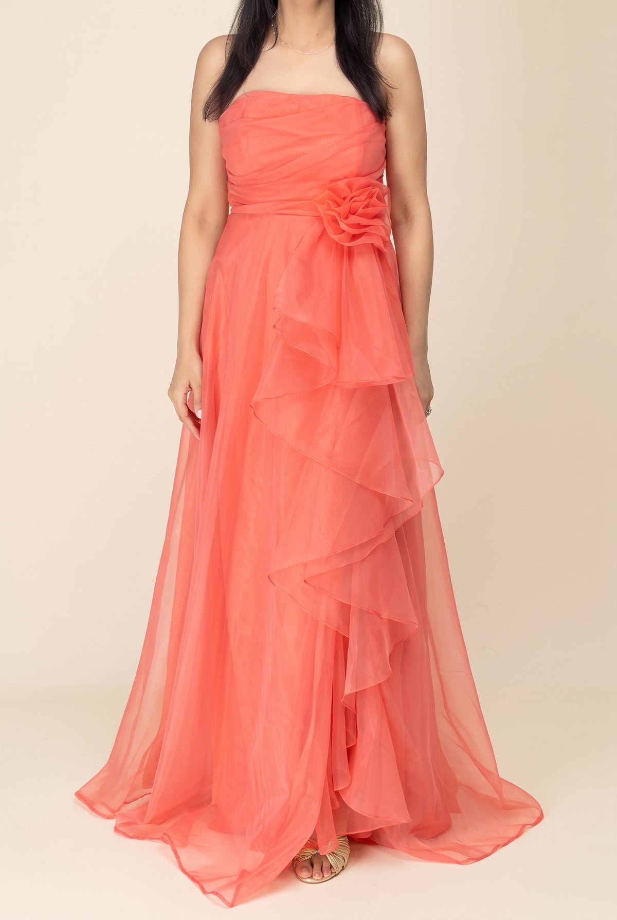 Front view of the coral organza maxi dress showing its strapless bodice, waist flower and full layered skirt.