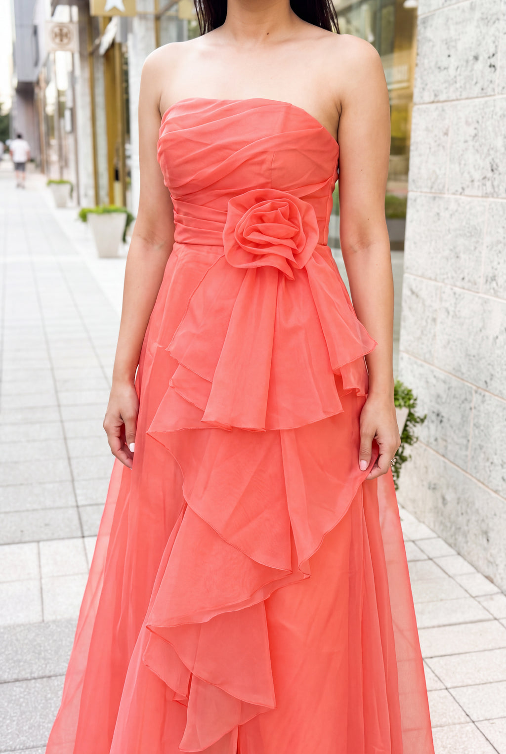 Close view of the coral dress showing bodice ruching, flower attachment, sheer ruffles and rolled edges.