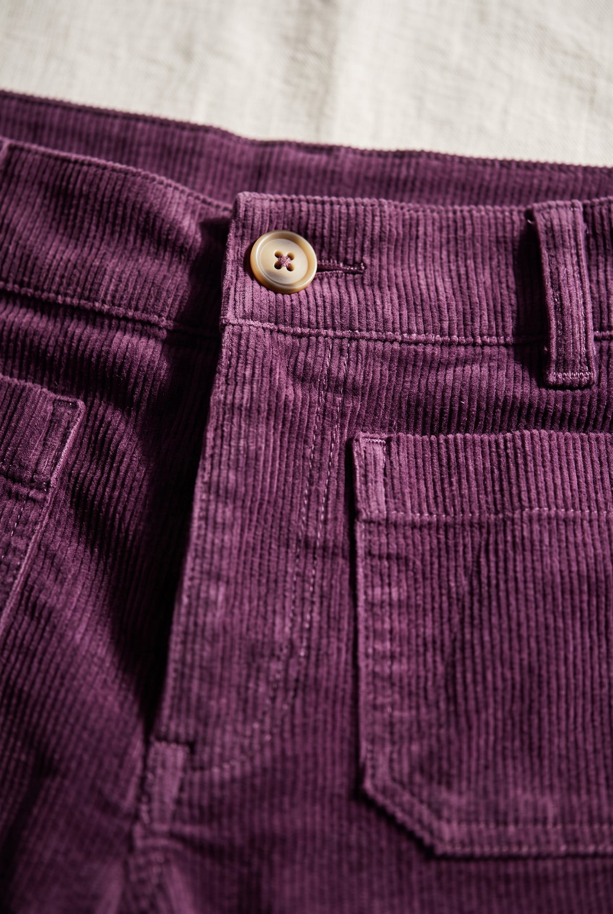 Close view of Rollin' With You corduroy pants showing the button, pocket stitching, and narrow purple ribs.