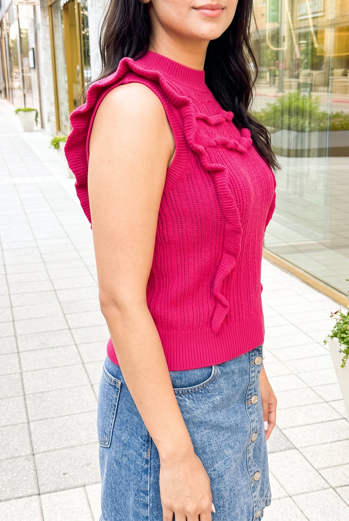 Angled side fit of the hot-pink sweater top showing armhole coverage, waist shape and projecting ruffles.