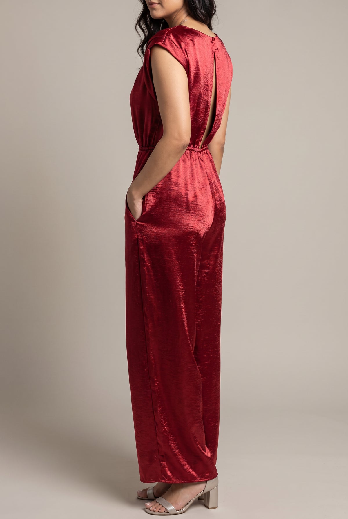 Angled view of the I'm Yours red satin jumpsuit showing its cap sleeve, pocket and wide-leg drape.