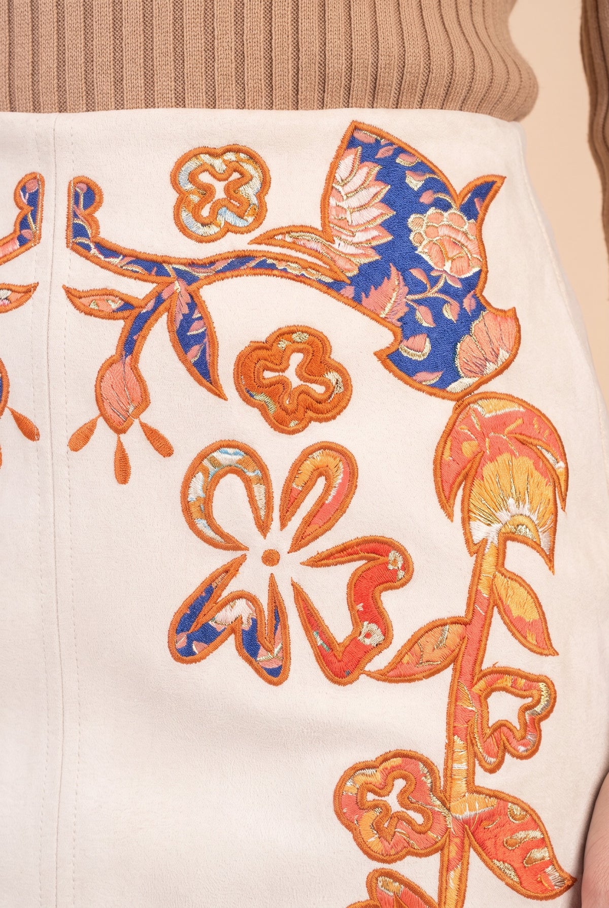 Close-up of the cream embroidered faux suede mini skirt showing the fabric and finishing details.