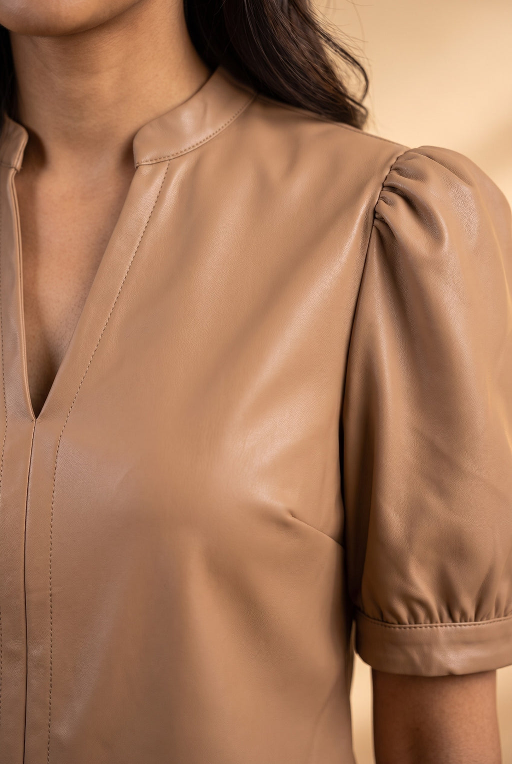 Close-up of the latte split neck faux leather top showing the fabric and finishing details.