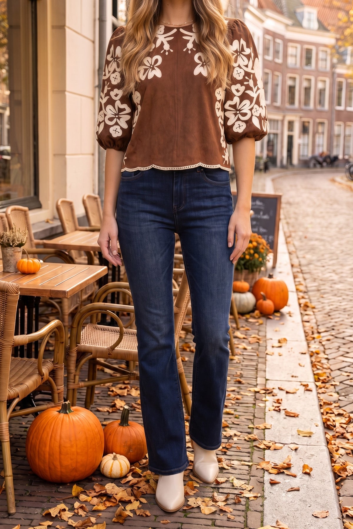 The embroidered suede top styled with dark indigo flare jeans, cream western booties and a delicate pearl chain necklace on a fall café terrace.