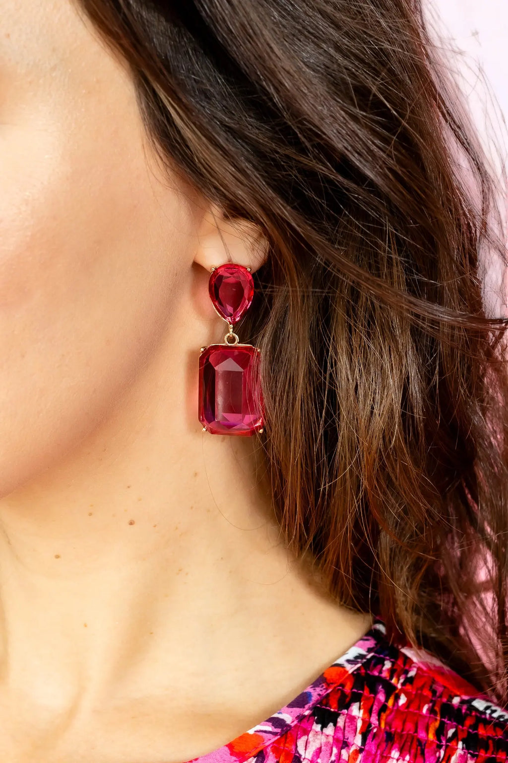 Bold pink gemstone statement drop earrings with gold-plated metal setting displayed on a jewelry stand.