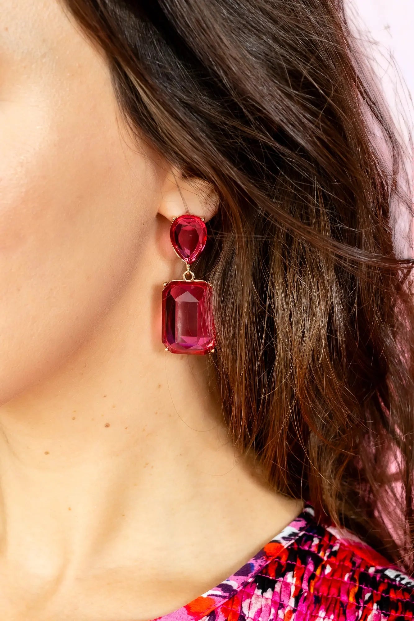 Bold pink gemstone statement drop earrings with gold-plated metal setting displayed on a jewelry stand.