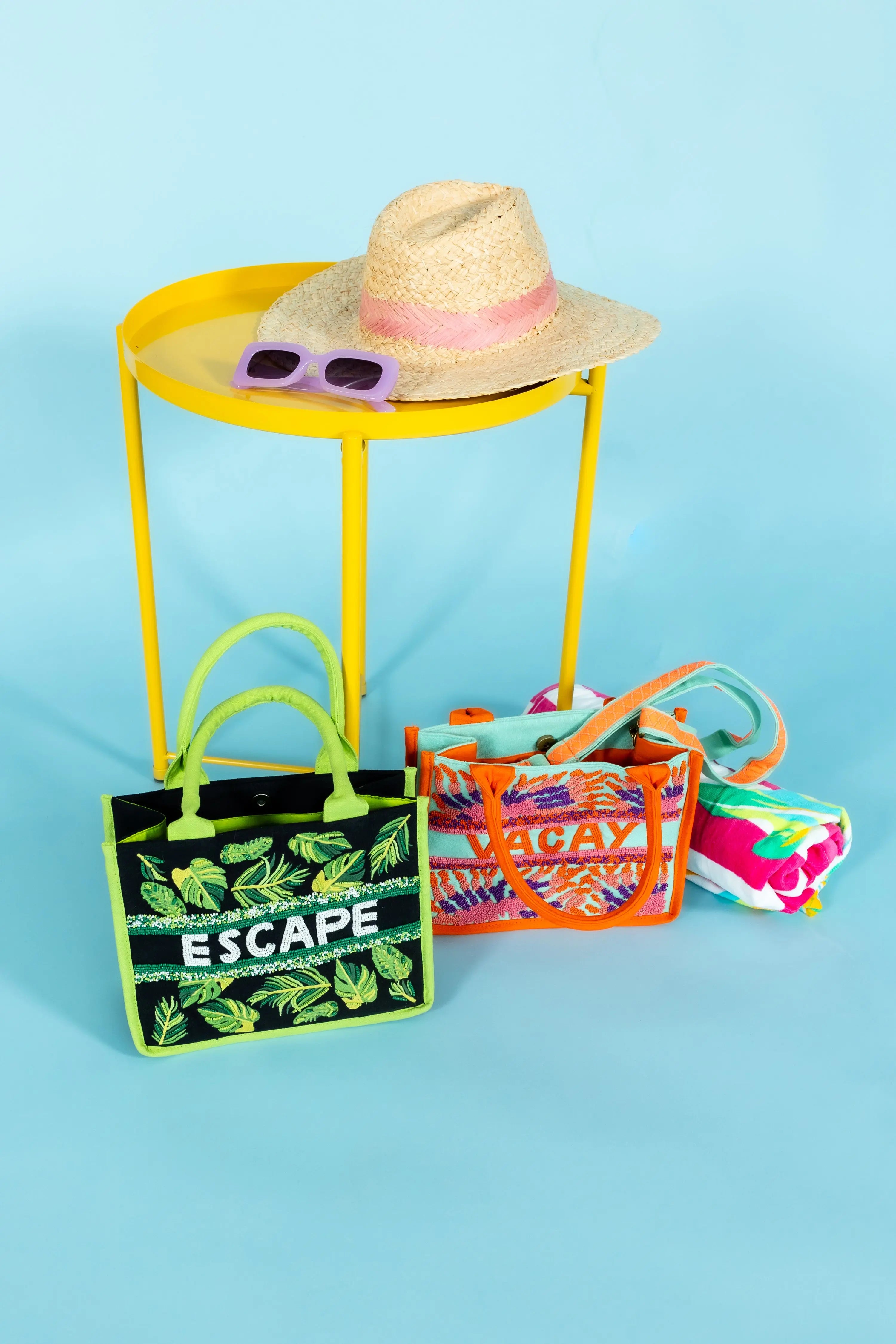 A tropical-themed tote bag featuring green leaf embroidery, sequin "ESCAPE" lettering, fabric-wrapped handles, and a detachable crossbody strap.