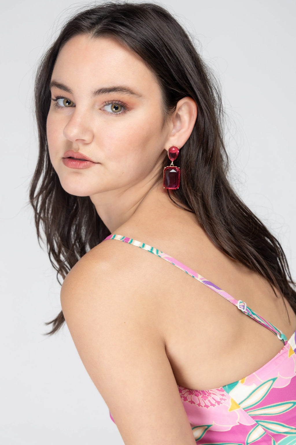 Bold pink gemstone statement drop earrings with gold-plated metal setting displayed on a jewelry stand.