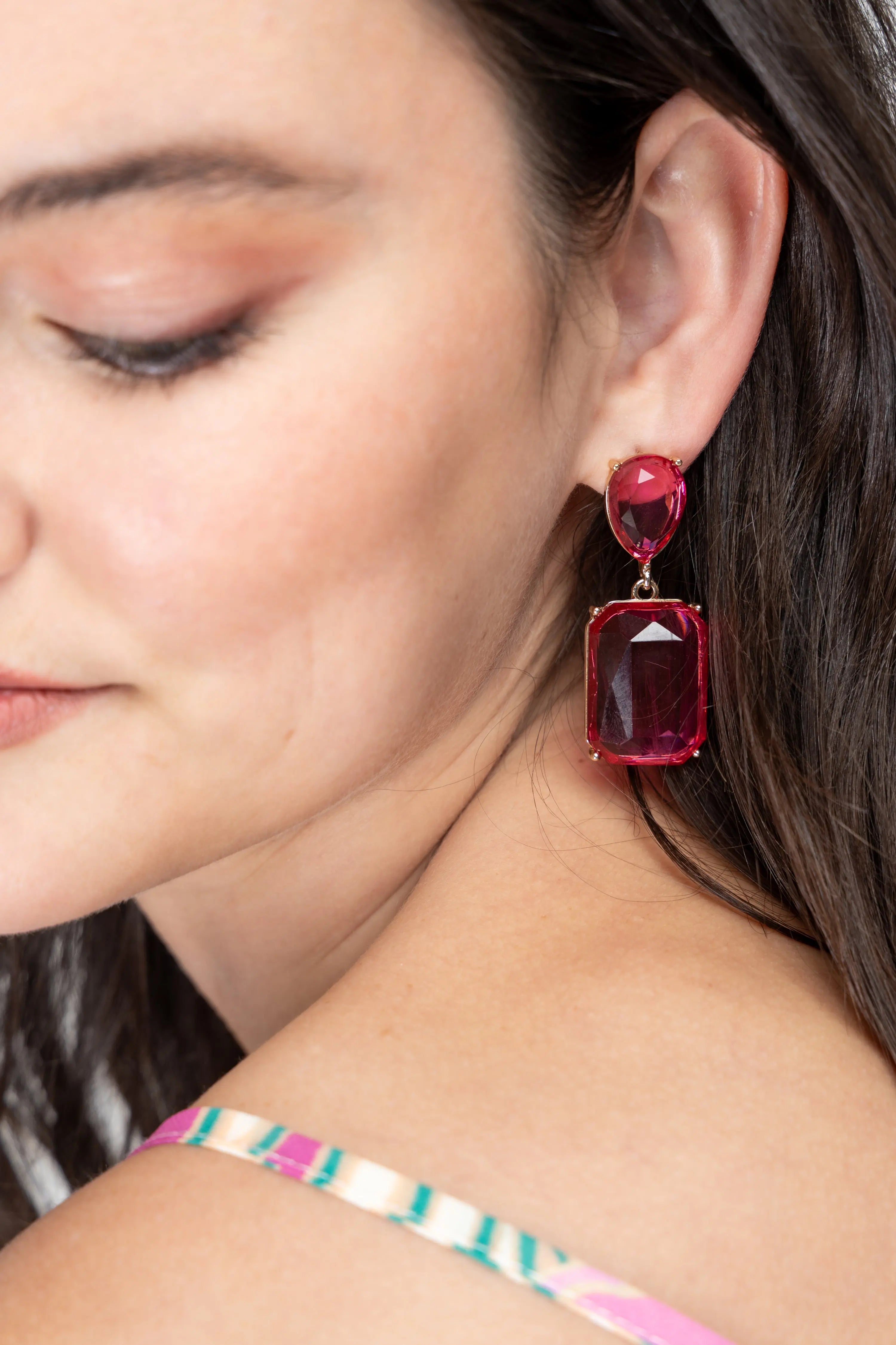 Bold pink gemstone statement drop earrings with gold-plated metal setting displayed on a jewelry stand.