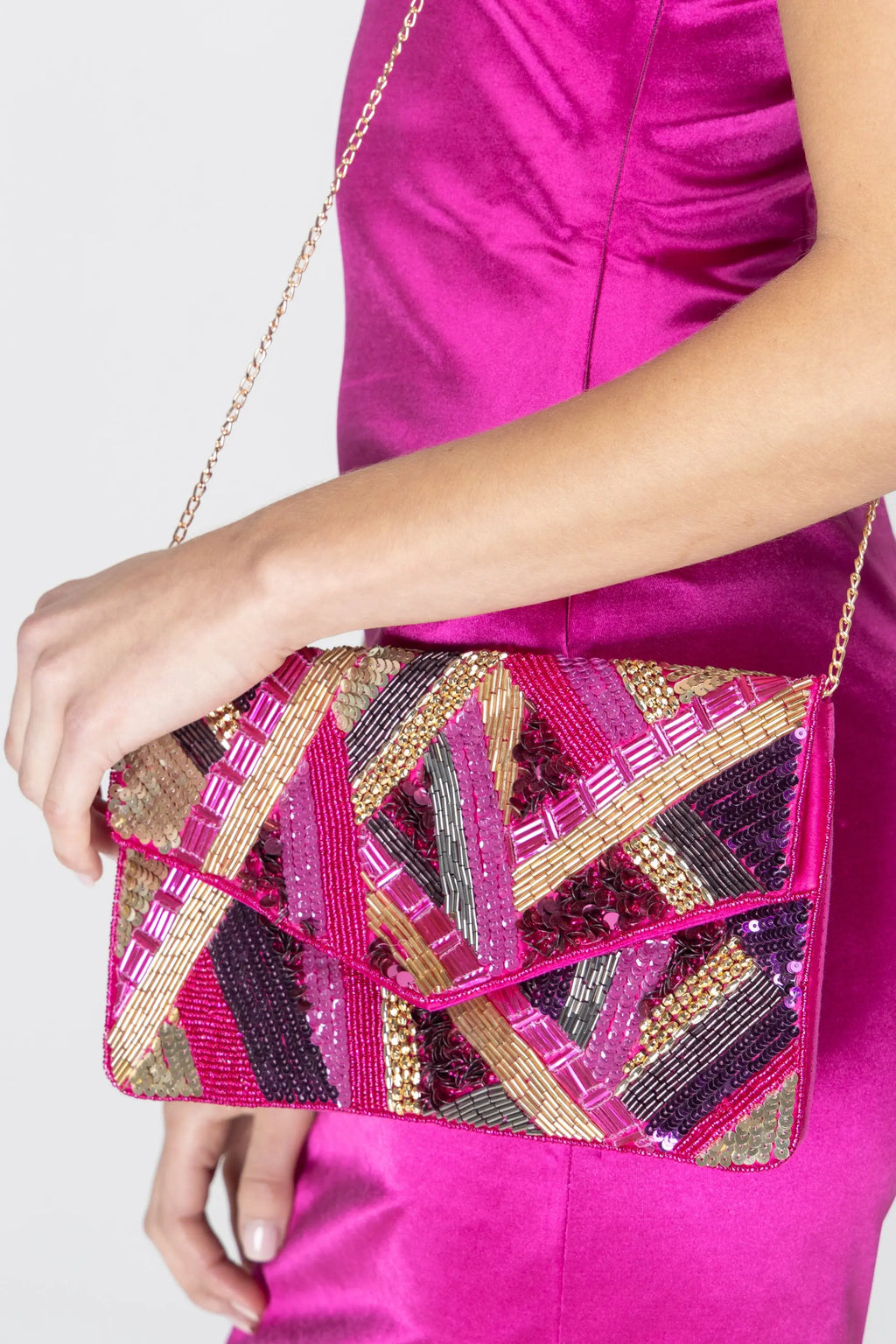 A dazzling fuchsia and gold hand-beaded clutch with intricate sequin details, featuring an envelope design and a gold-tone chain strap for versatile styling.
