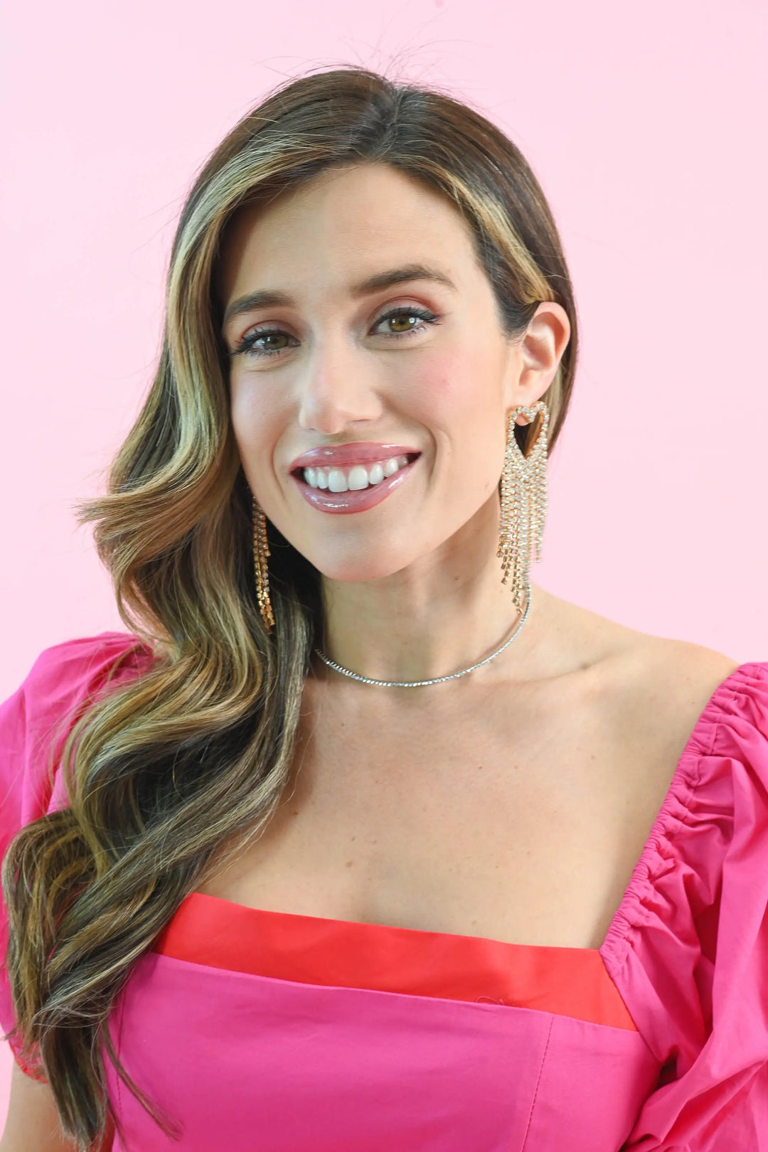 Woman wearing radiant heart fringe rhinestone earrings with cascading rhinestones, styled with an off-shoulder pink dress.