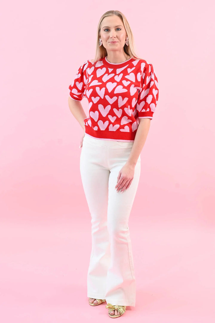 Woman wearing a red heart print puff sleeve sweater with white jeans, perfect for a chic and cozy Valentine's Day outfit.