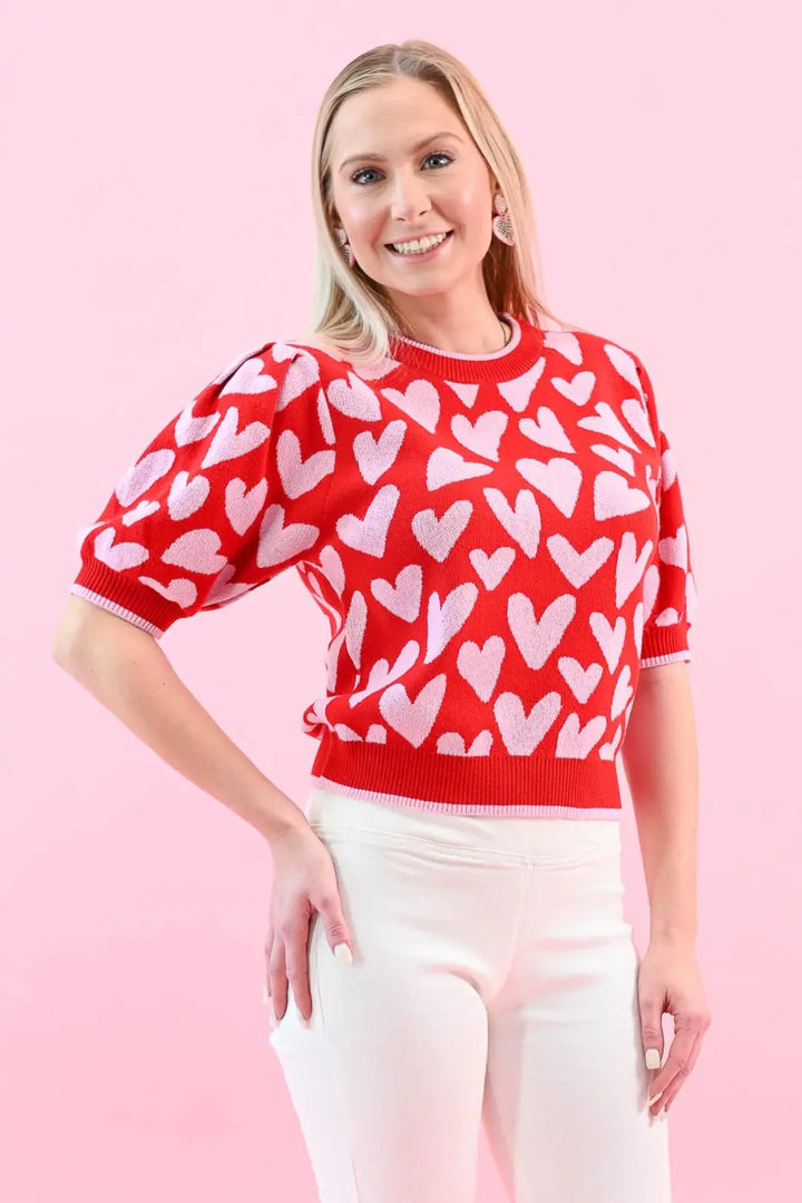 Woman wearing a red heart print puff sleeve sweater with white jeans, perfect for a chic and cozy Valentine's Day outfit.