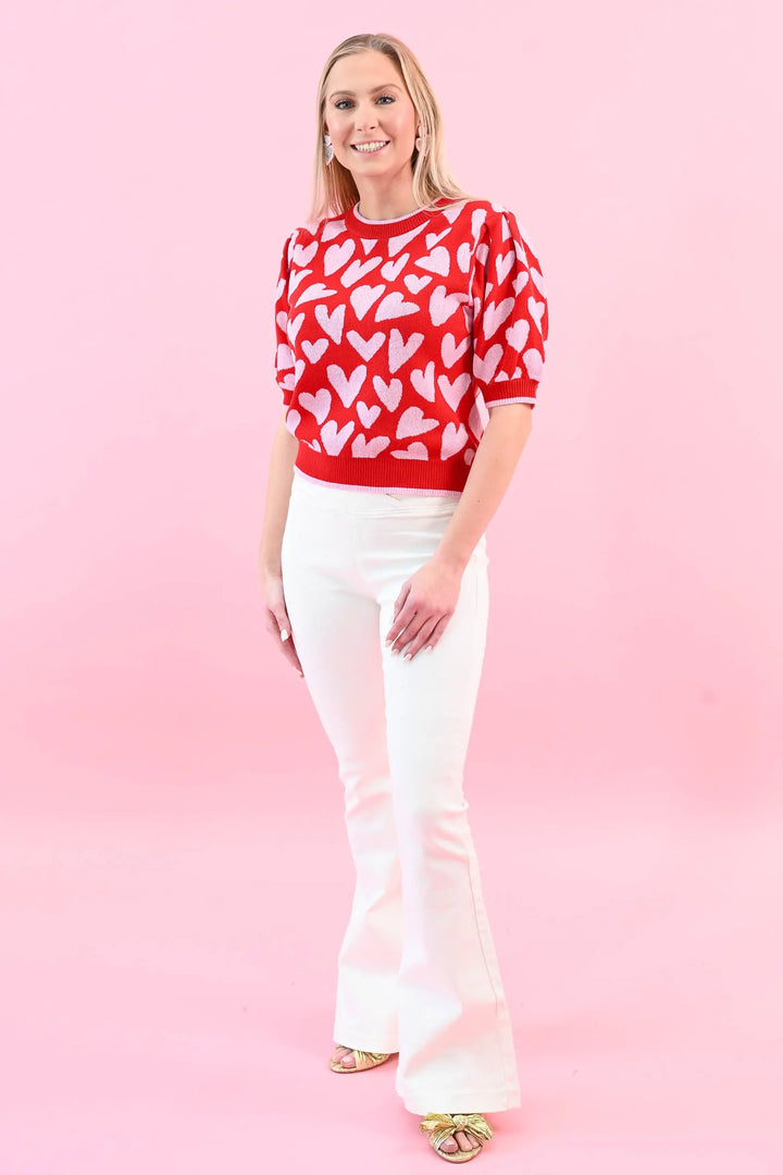 Woman wearing a red heart print puff sleeve sweater with white jeans, perfect for a chic and cozy Valentine's Day outfit.