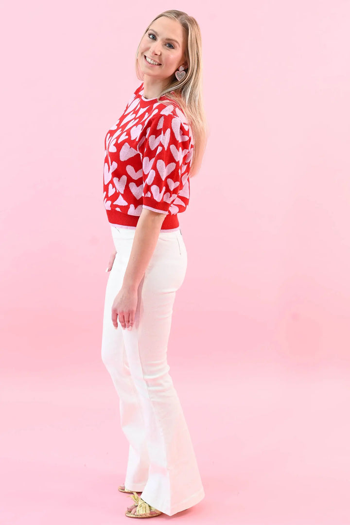 Woman wearing a red heart print puff sleeve sweater with white jeans, perfect for a chic and cozy Valentine's Day outfit.