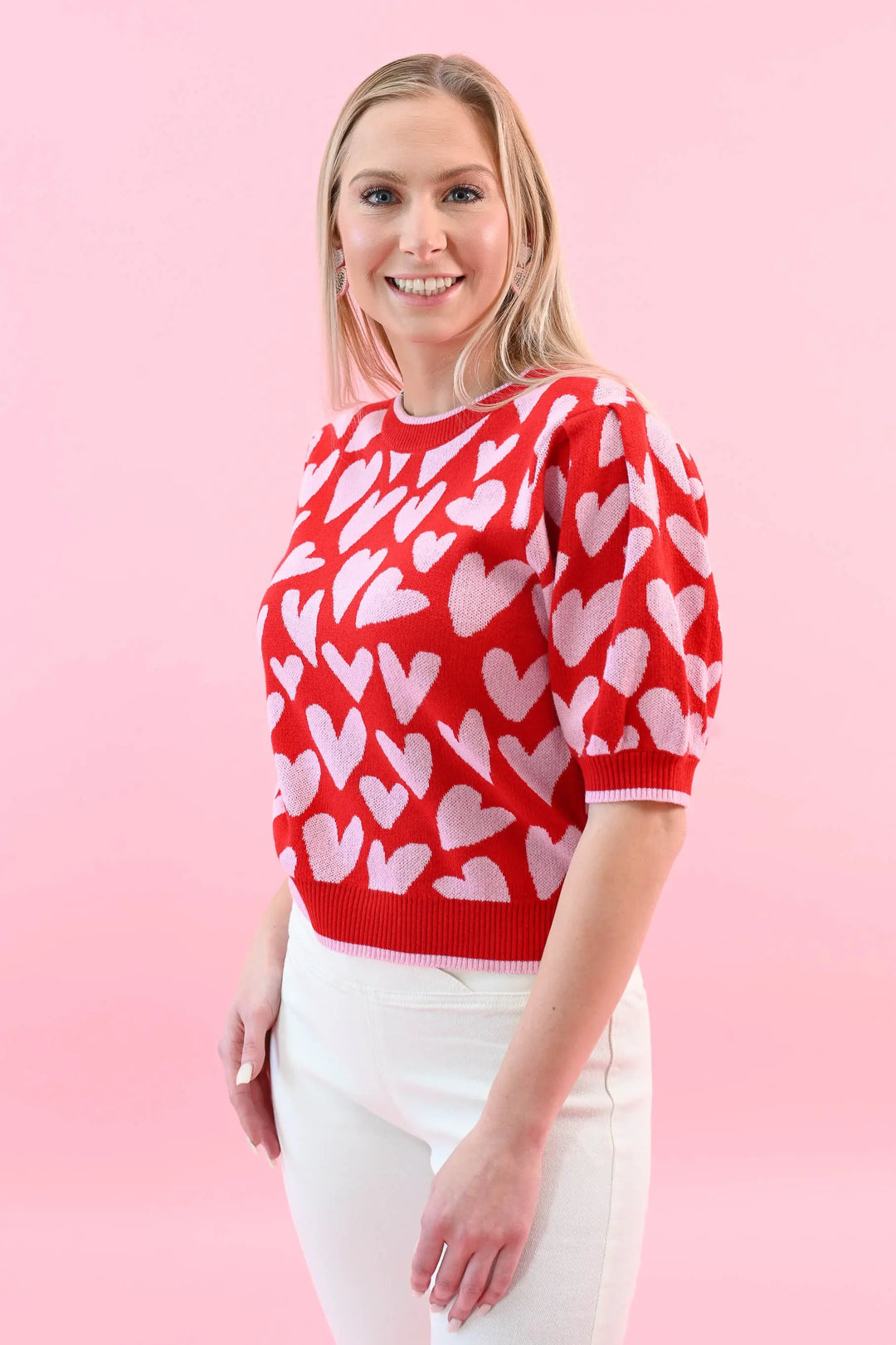 Woman wearing a red heart print puff sleeve sweater with white jeans, perfect for a chic and cozy Valentine's Day outfit.