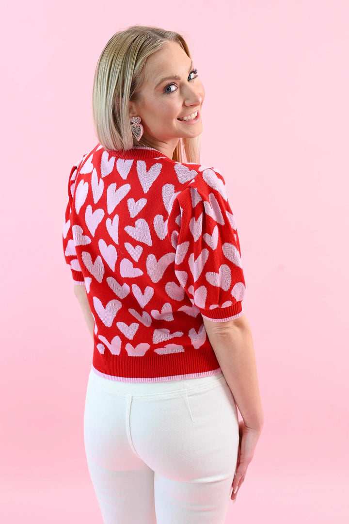 Woman wearing a red heart print puff sleeve sweater with white jeans, perfect for a chic and cozy Valentine's Day outfit.