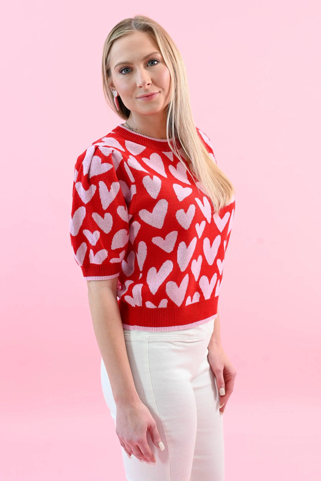 Woman wearing a red heart print puff sleeve sweater with white jeans, perfect for a chic and cozy Valentine's Day outfit.