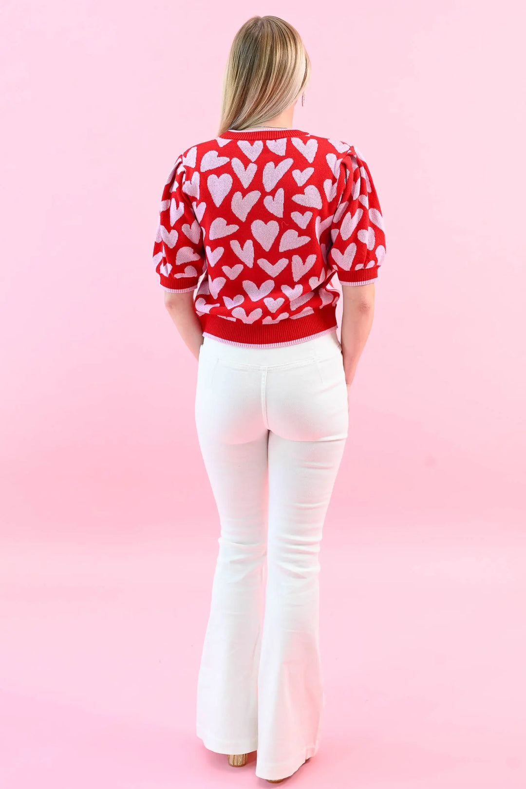 Woman wearing a red heart print puff sleeve sweater with white jeans, perfect for a chic and cozy Valentine's Day outfit.