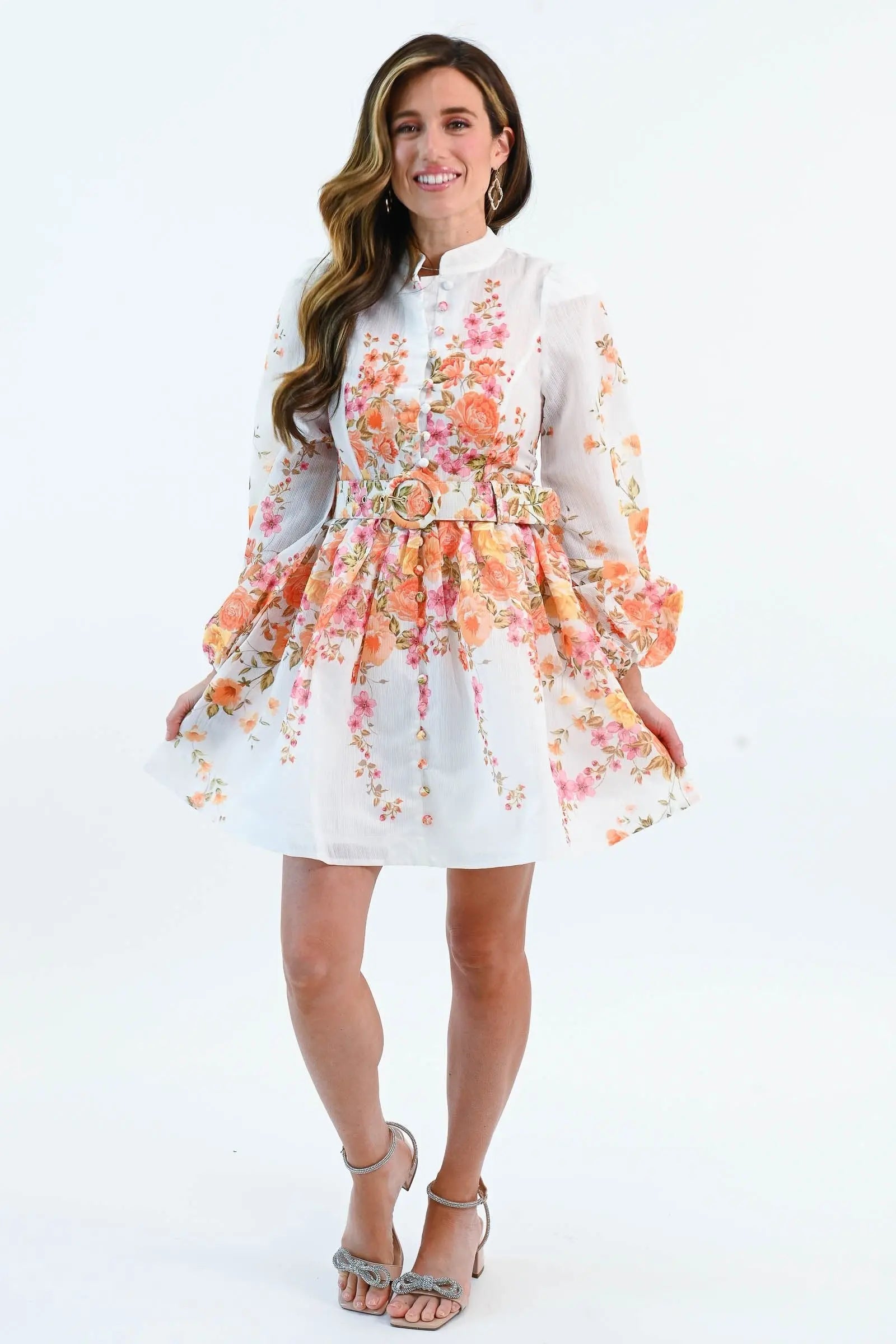 A woman wearing a floral chiffon mini dress with puff sleeves, a belted waist, and a button-down front, perfect for spring and summer.