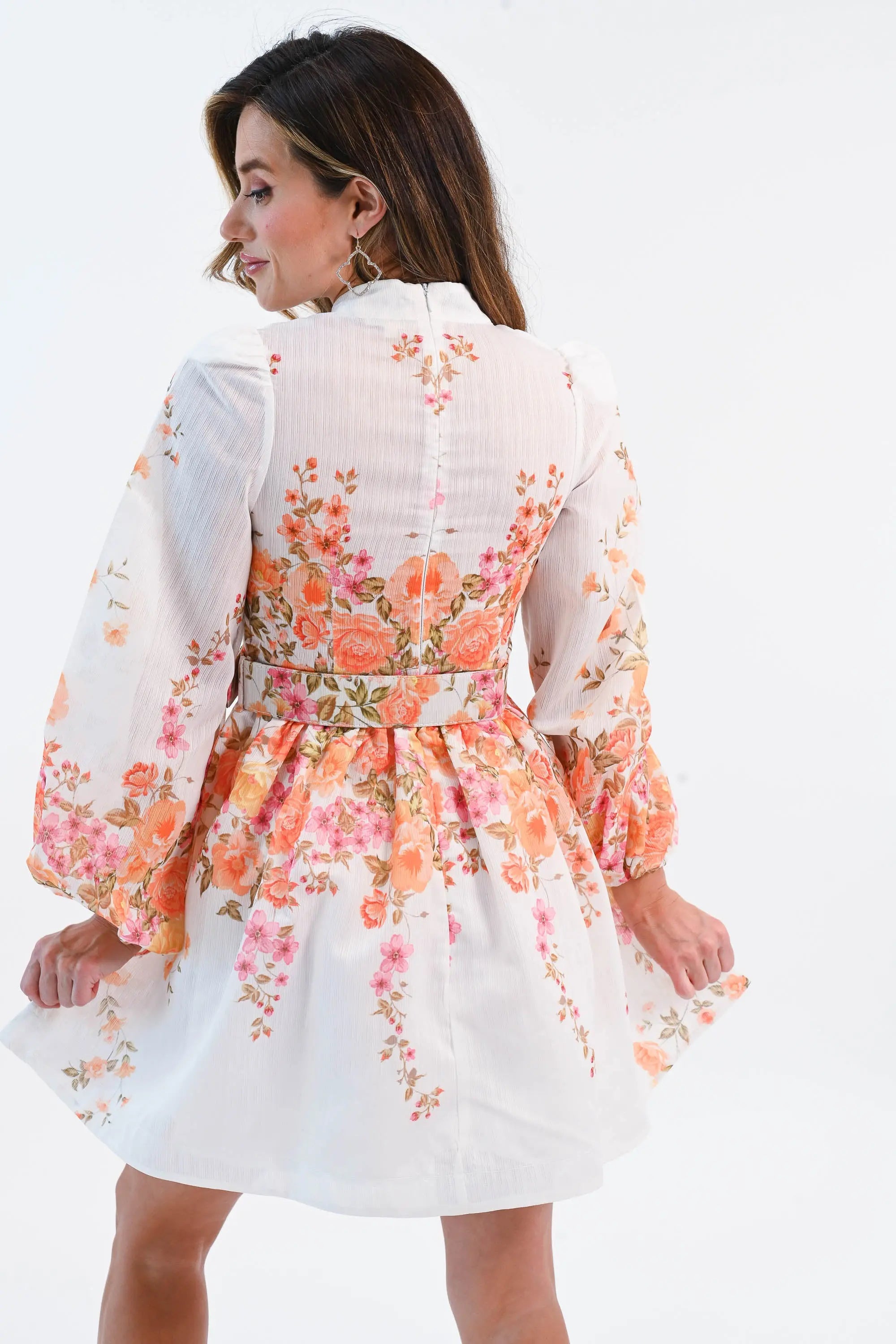 A woman wearing a floral chiffon mini dress with puff sleeves, a belted waist, and a button-down front, perfect for spring and summer.