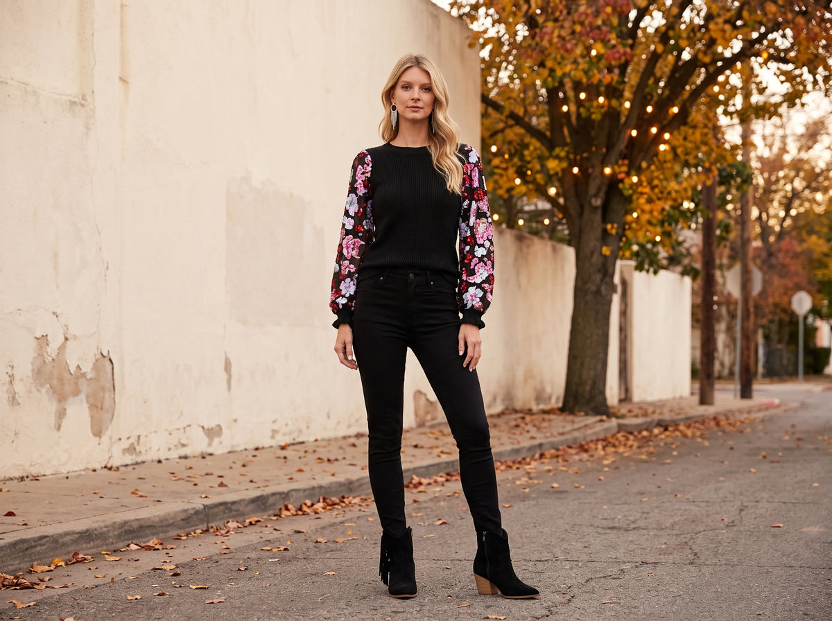 A woman in a black sweater with floral sequin sleeves, black skinny jeans and black fringe ankle boots on an autumn street