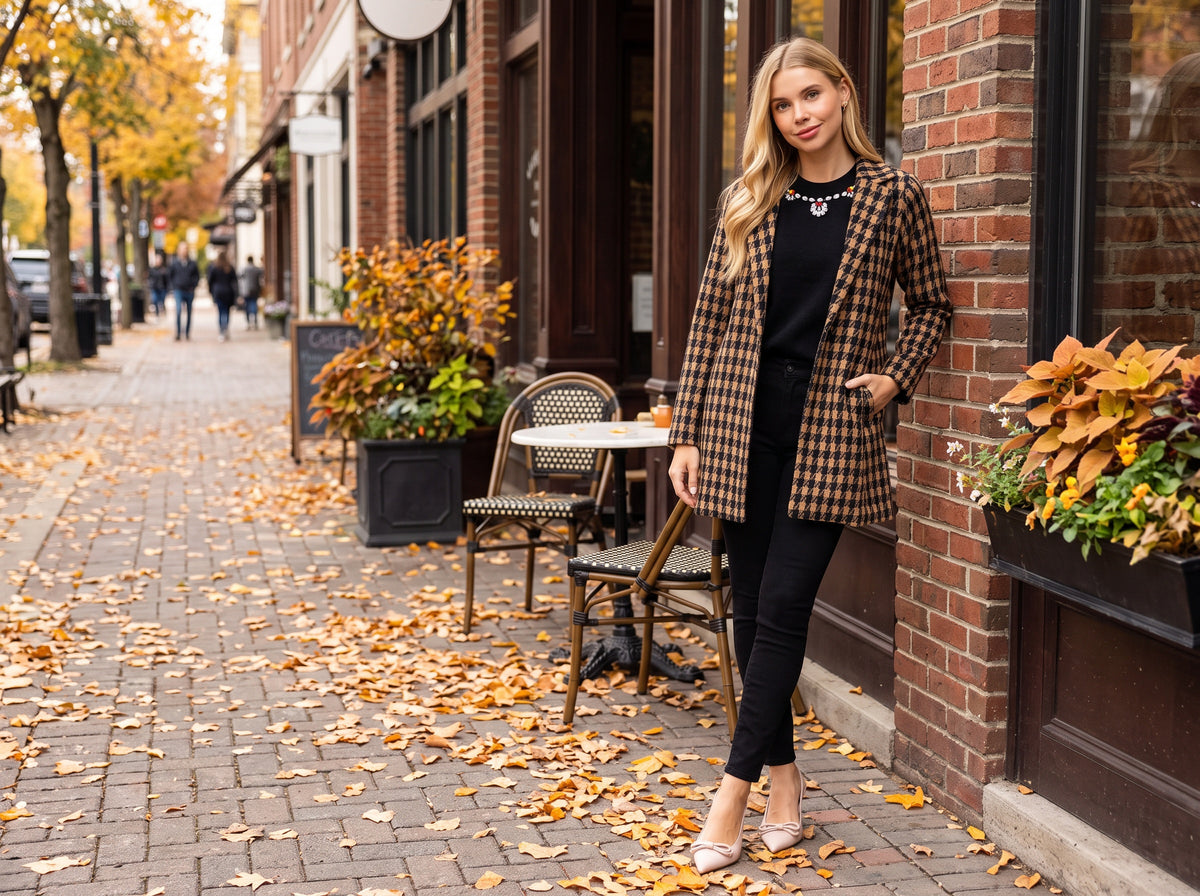 A woman in a brown houndstooth one-button jacket over a black jewel-neck sweater, black skinny jeans and nude pumps, outside a brick cafe in autumn