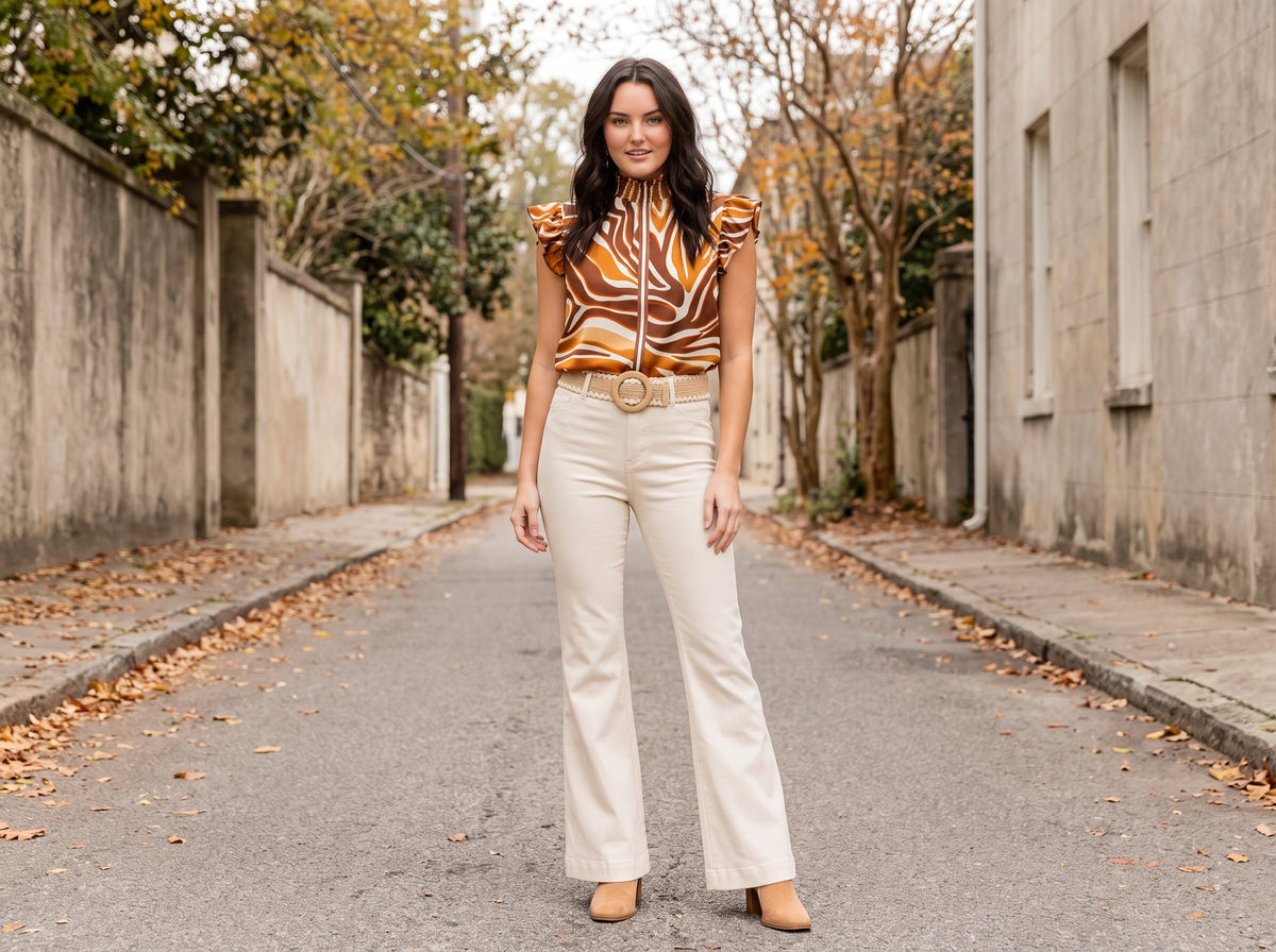 A woman in a brown striped satin top, cream flare jeans with a braided wooden-buckle belt and tan booties