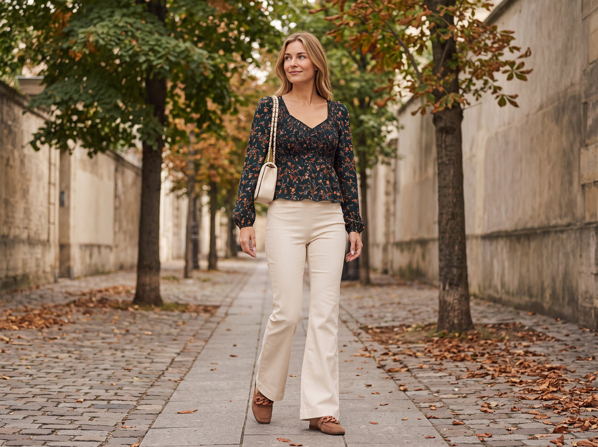 A woman in a dark floral sweetheart-neck top, cream flare jeans and brown suede mules with a cream quilted bag