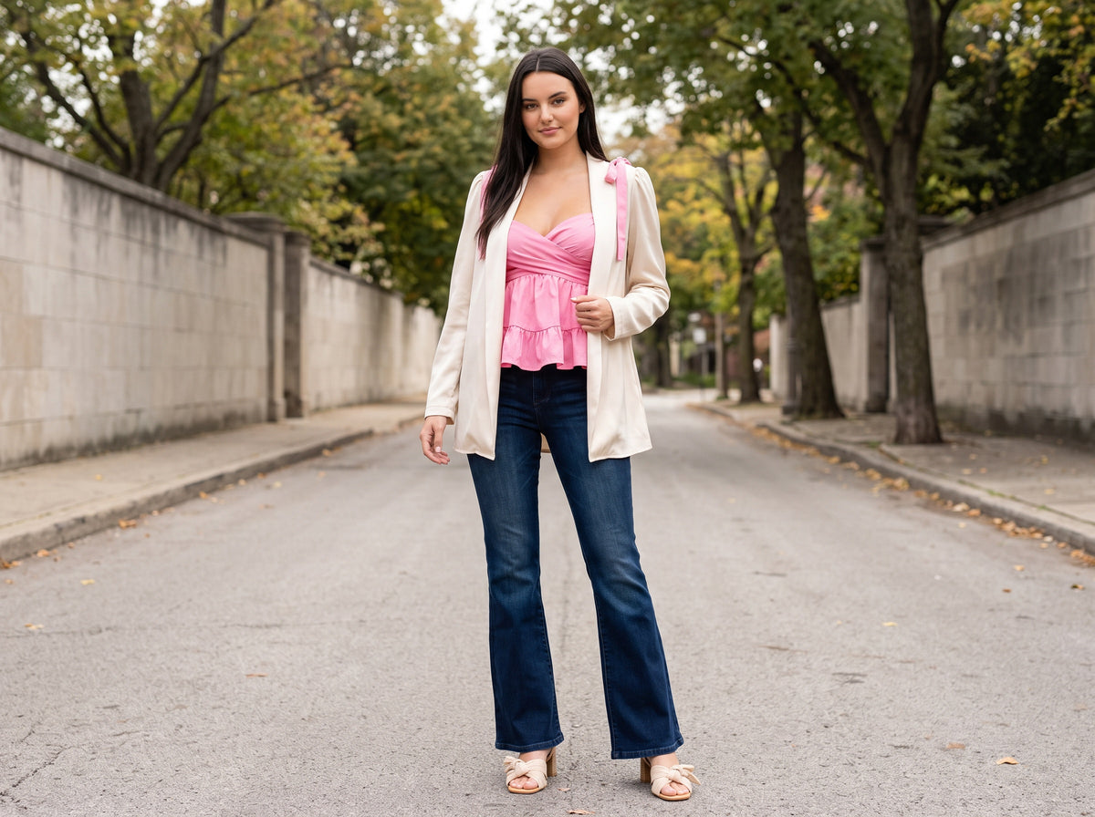 A woman in a pink bow-detail top under an ivory cardigan blazer, dark flare jeans and bow sandals