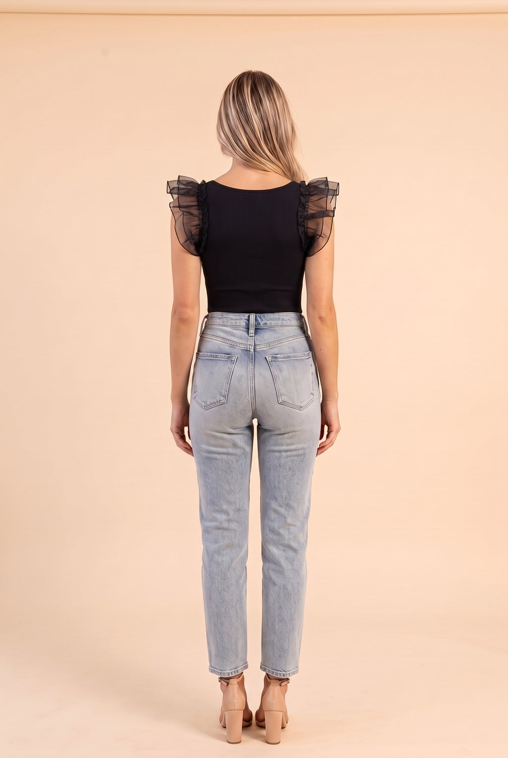 Back view of the black ribbed bodysuit with sheer ruffle sleeves, worn with light blue jeans on a cream backdrop