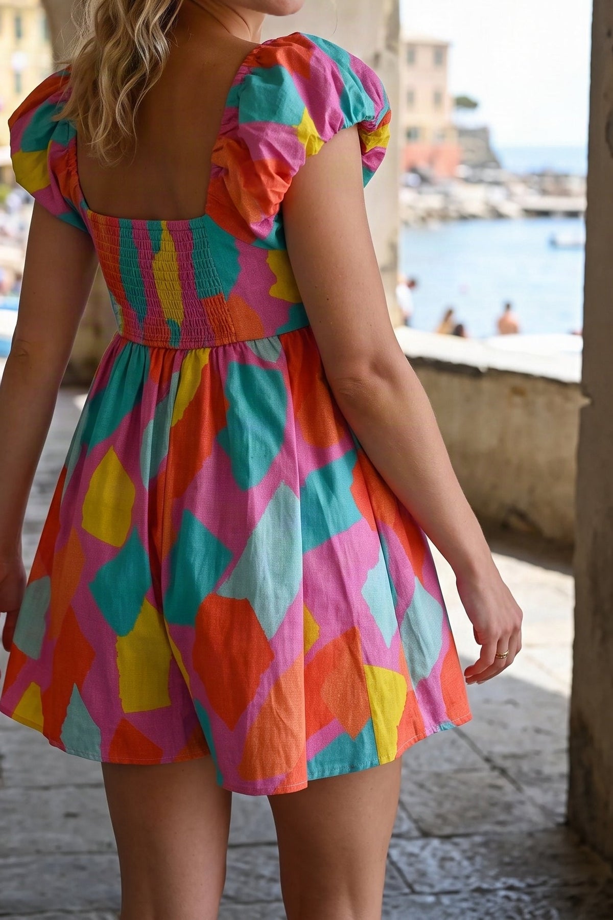 Back view of the multicolour print puff-sleeve romper dress by the sea, from the chin down