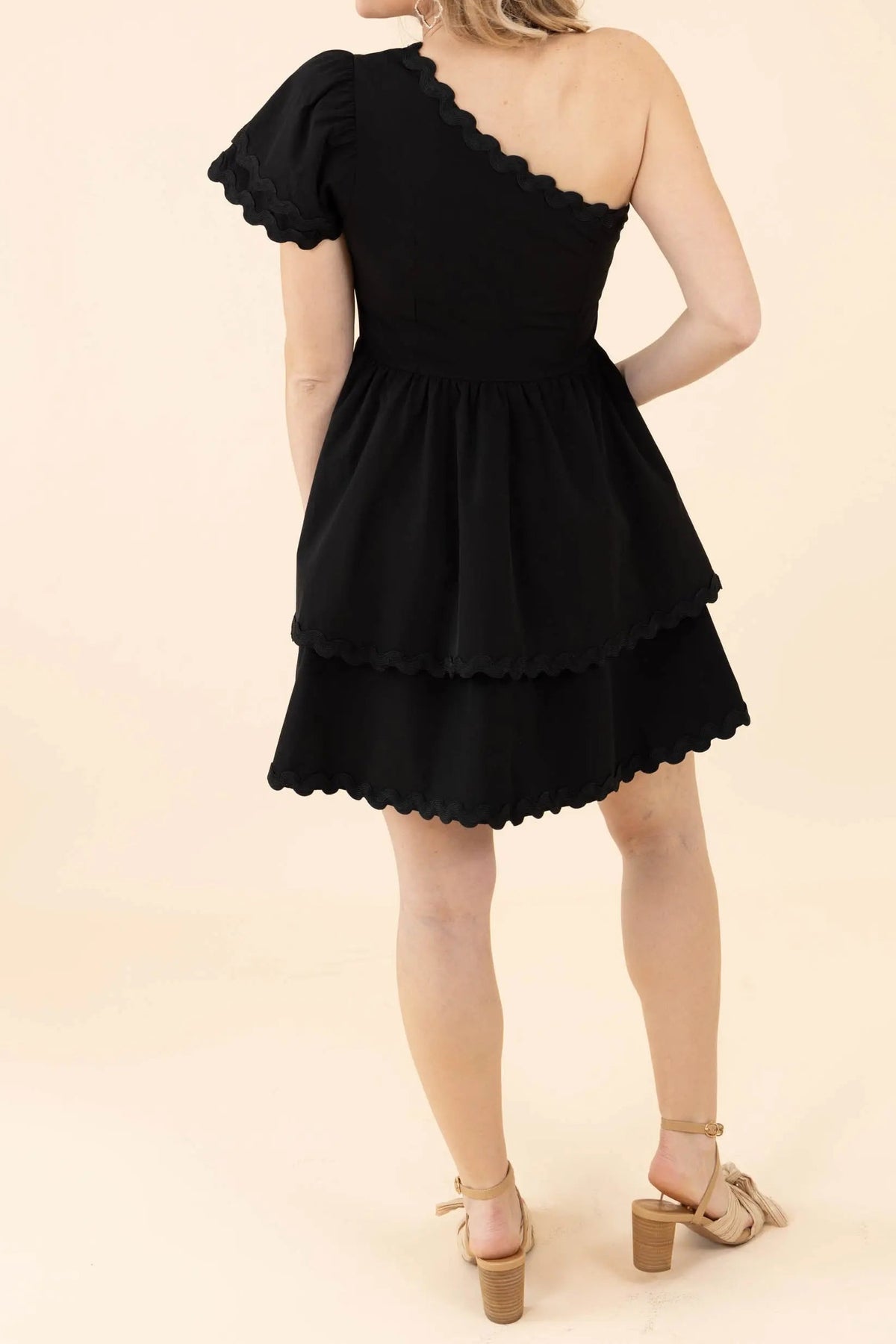 Back of the black one-shoulder mini dress, showing the diagonal scalloped back neckline and tiered skirt
