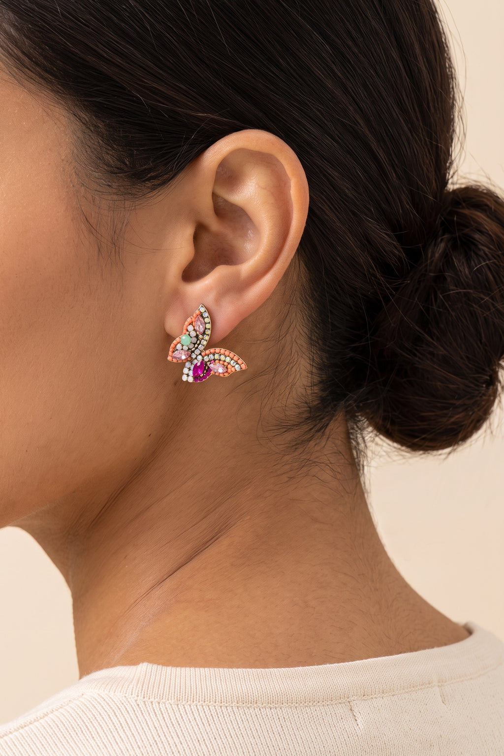 June Butterfly Earrings in Pink worn on the earlobe at true size: a small half-butterfly stud about 1 in across